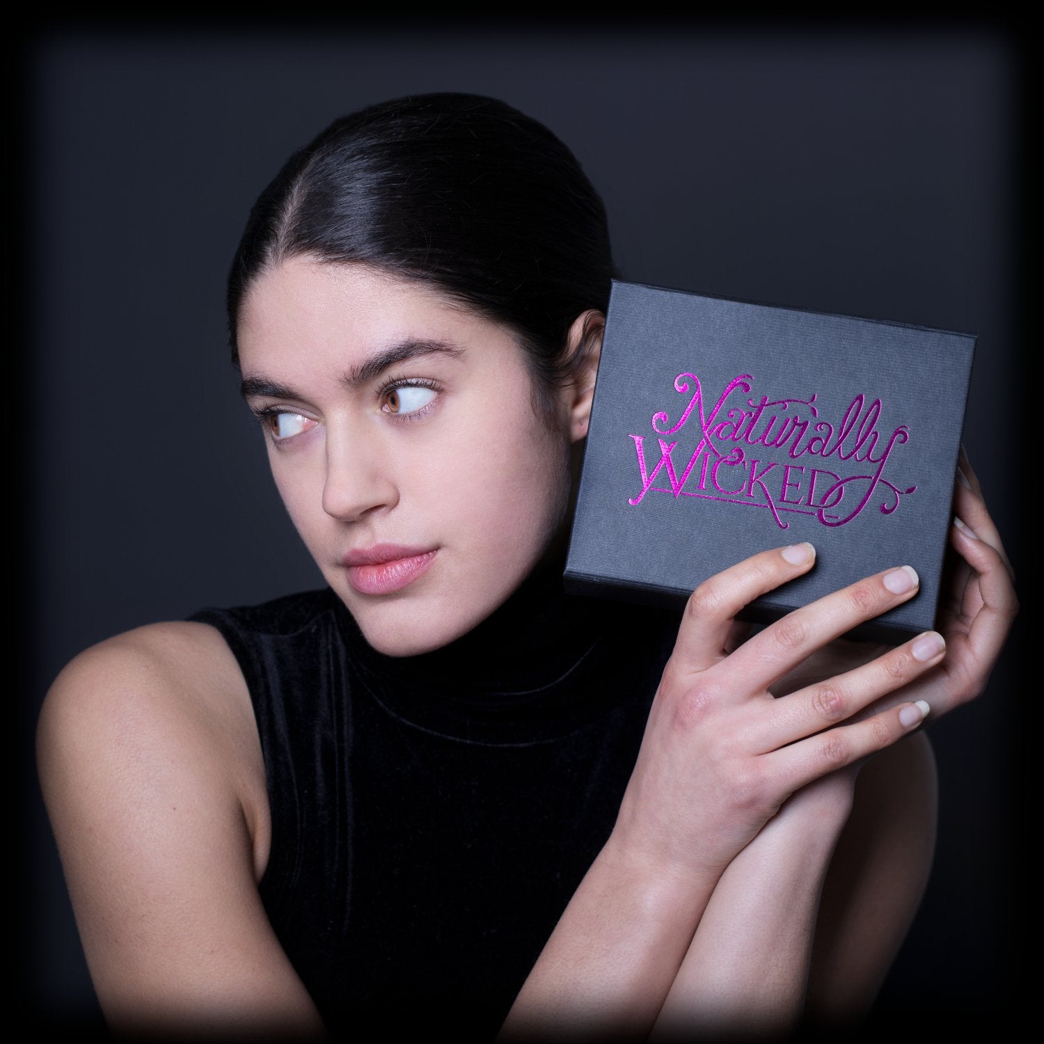 Brunette model holding a Naturally Wicked gift box with vibrant pink branding